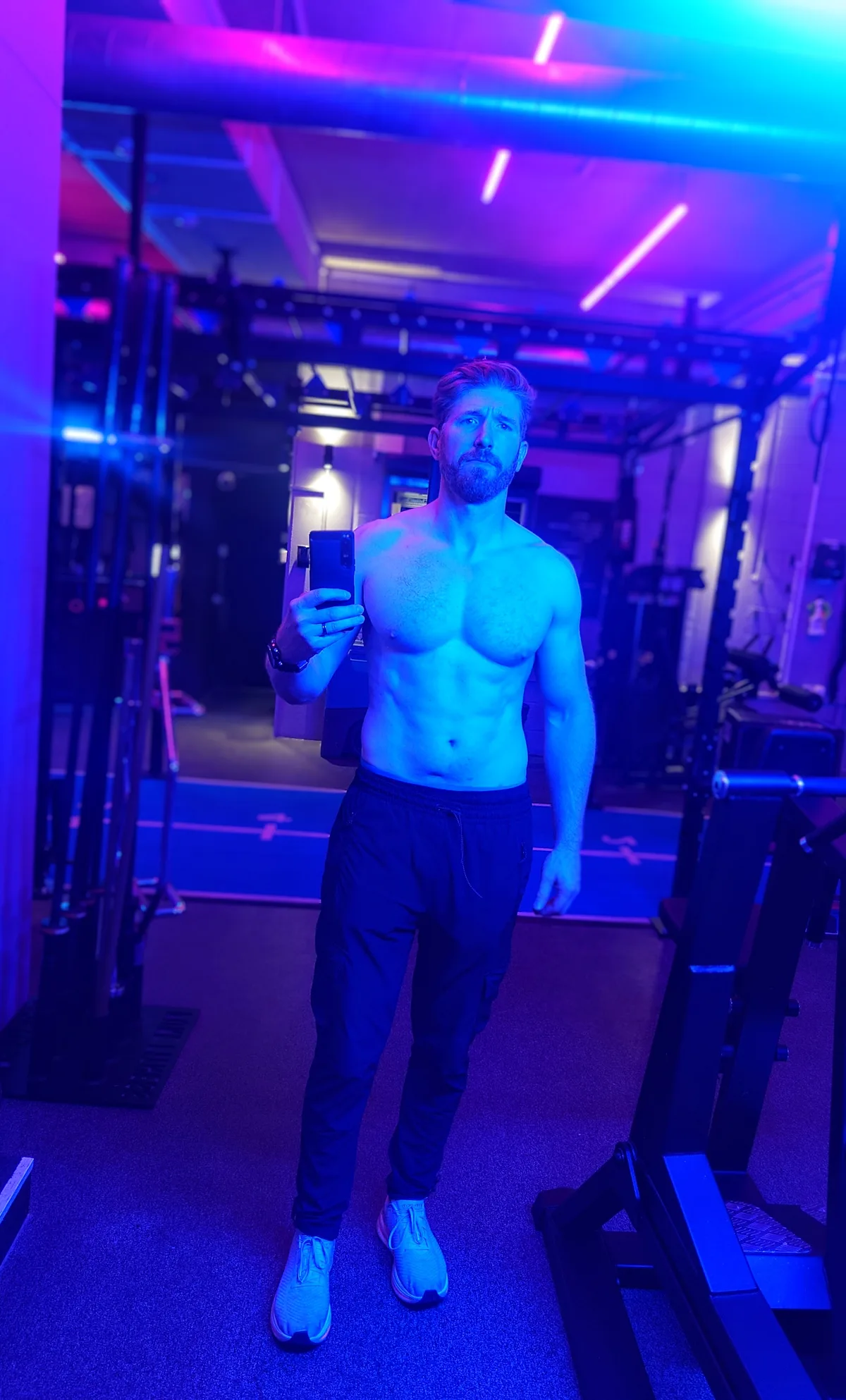 Man taking a mirror photo in a gym lit with blue and purple lights